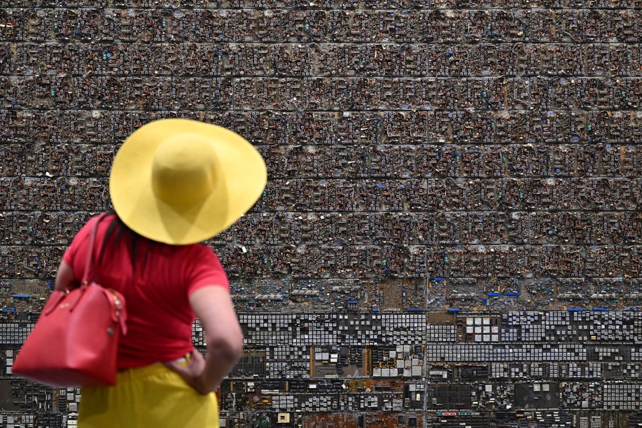 A person looks at a work of art—a wall covered in electronic components, looking much like a dense cityscape seen from above.