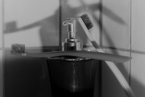 a black and white photo of two toothbrushes leaning against a faucet, their shadows on the tiled wall behind them