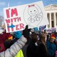 A person holds a sign saying "I'm With Her" with a drawing of a fetus on it.