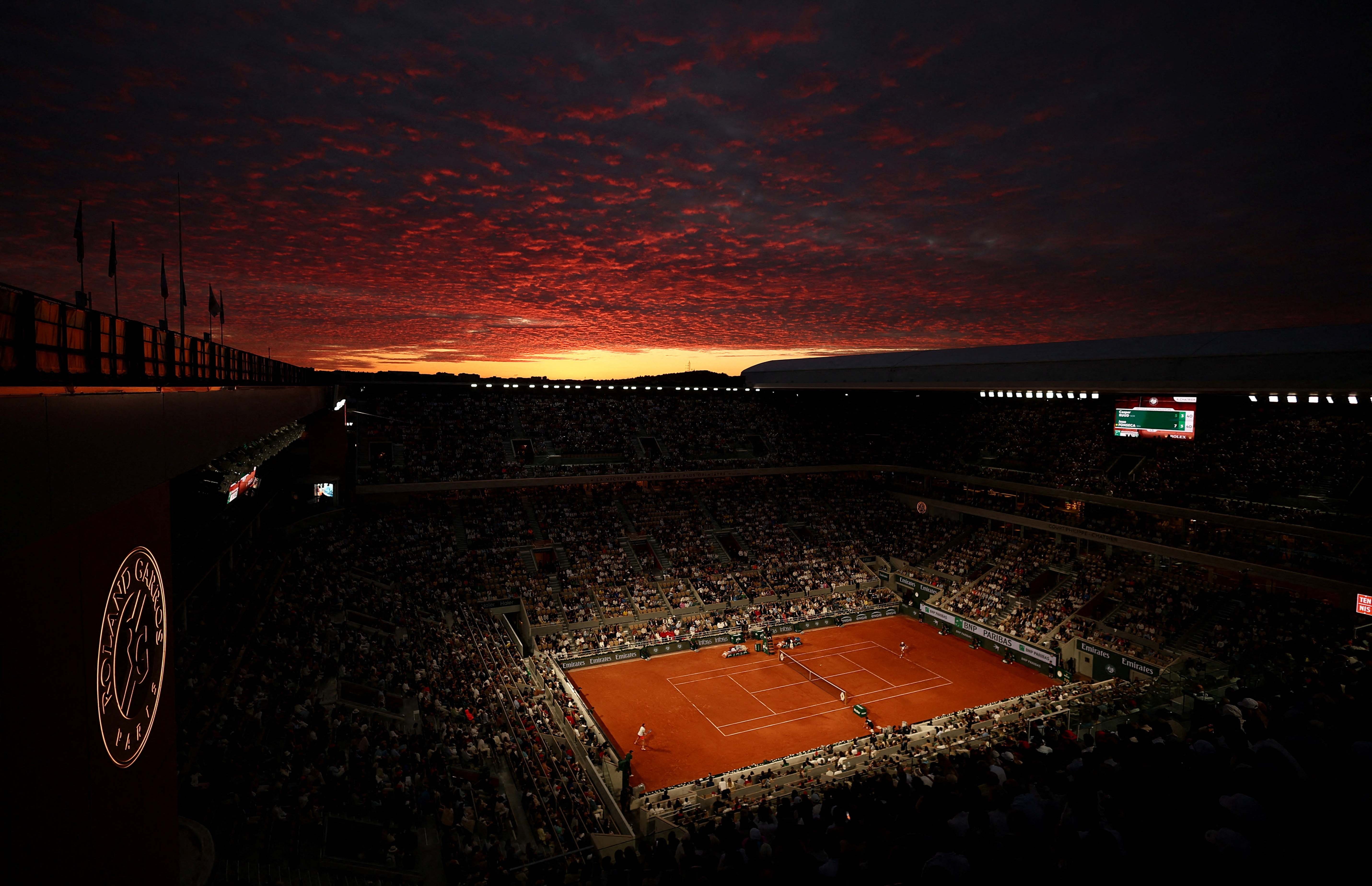 The sun sets over a tennis stadium during a match.