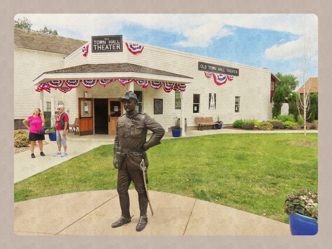 A statue of Theodore Roosevelt stands outside of a building and build stand nearby