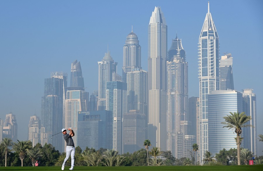 A man plays golf in front of the tall buildings of Dubai.