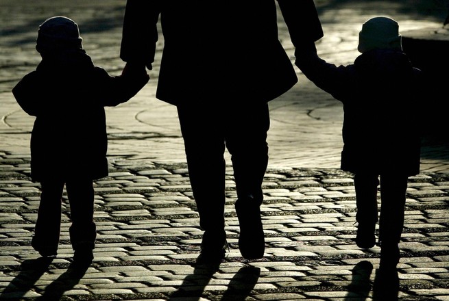 Silhouettes of two children and an adult holding their hands, walking on a brick road