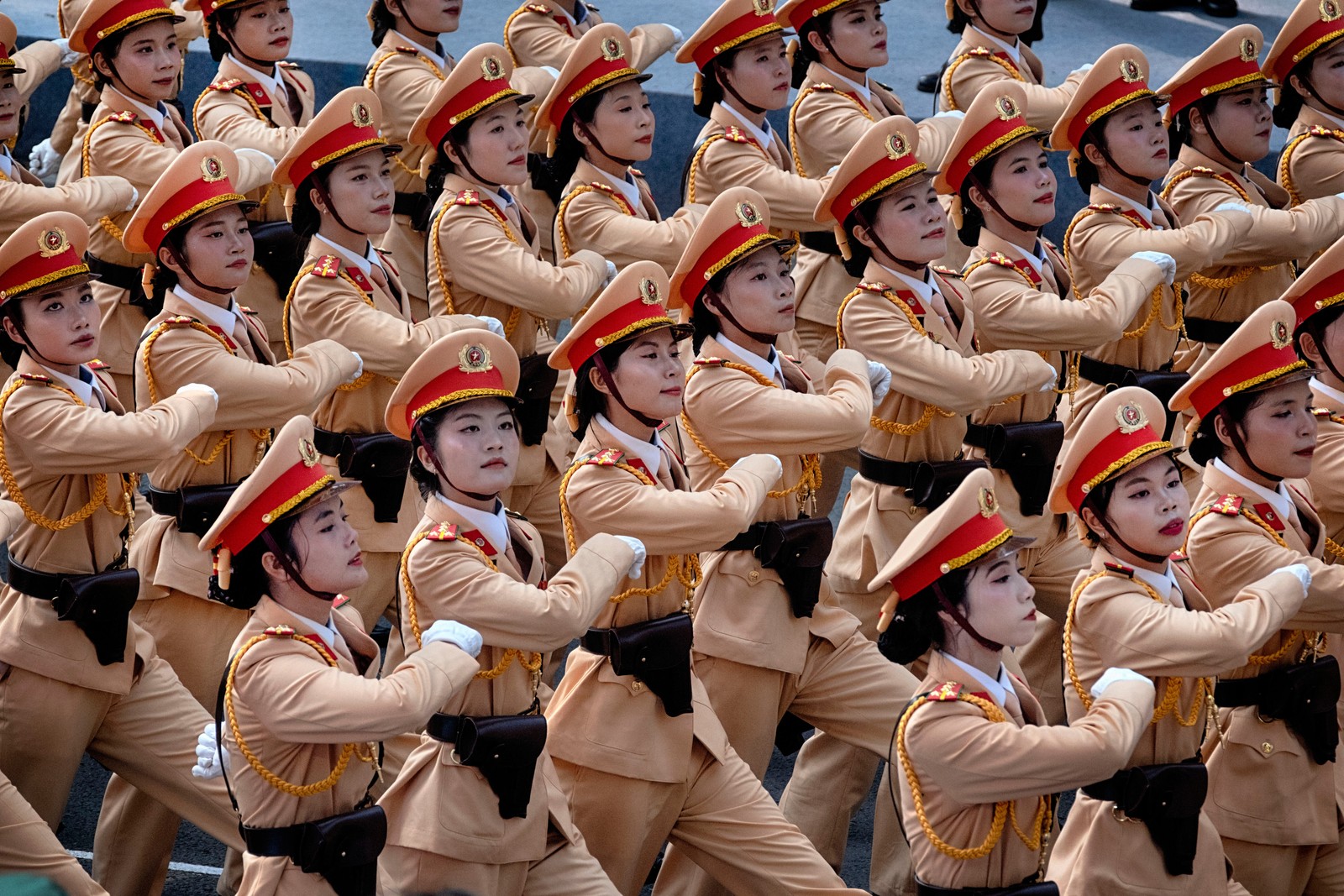 Police officers in dress uniforms march in formation during a parade in Vietnam.