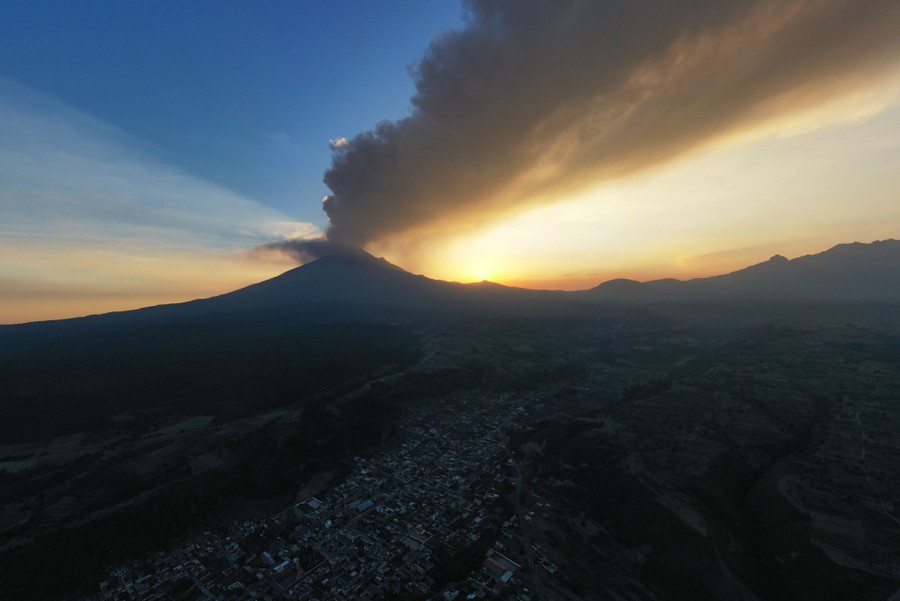 A plume of ash flows through the sky, emanating from a distant volcano.