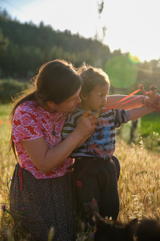 a woman teaches a boy to throw seeds using a slingshot