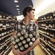 A young man walks down a wine aisle holding many cans.