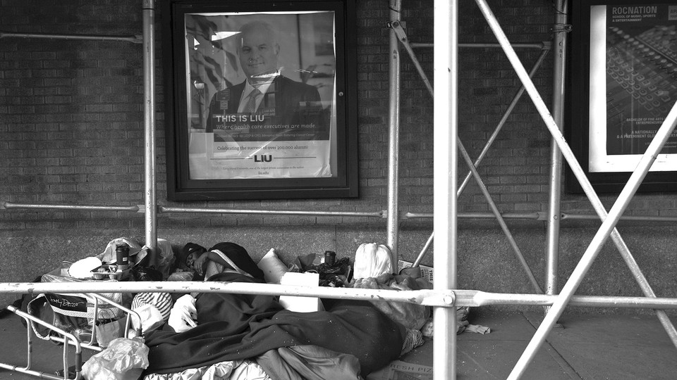 A pile of belongings on a city street, below a poster saying "This is where health executives are made"