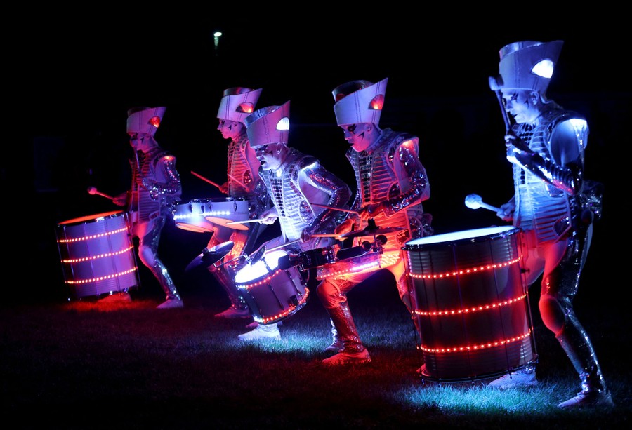 A team of five drummers in illuminated costumes performs.