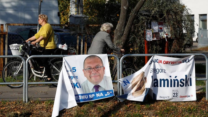 Women ride bicycles past election posters, a day after parliamentary election, in Raszyn