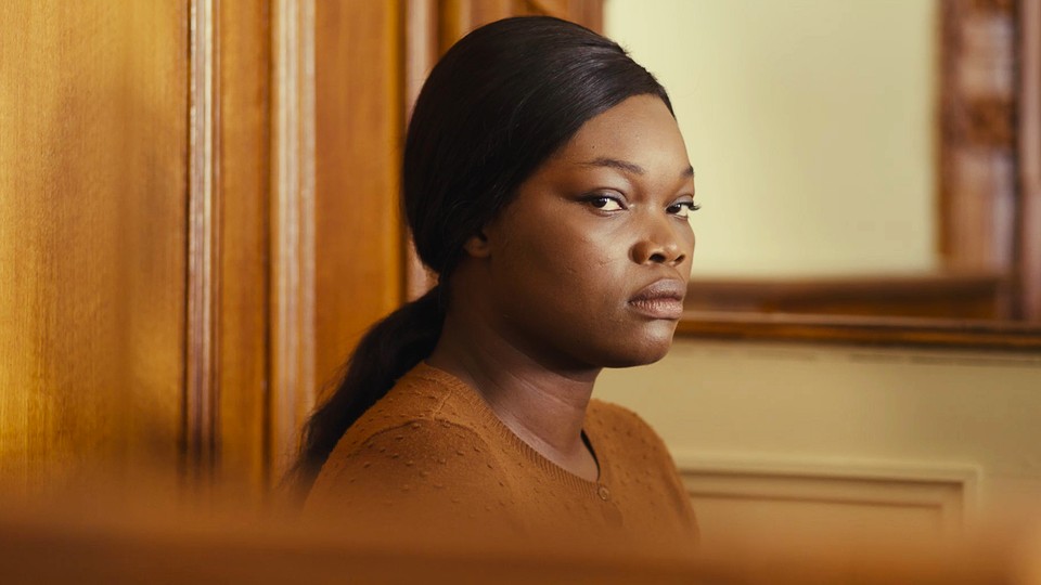 Guslagie Malanda staring directly at the camera while seated in a courtroom in "Saint Omer"