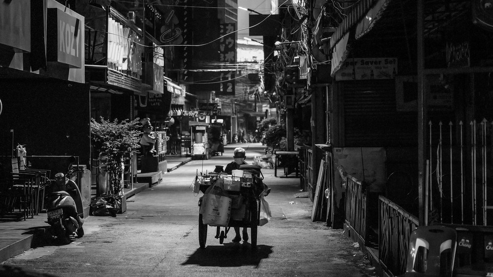 A woman pushes her food cart along an empty street in Bangkok