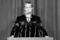 A white man in a suit stands on a podium, with his image so chopped up as to be uncrecognizable