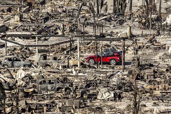 A single undamaged red car sits in a ruined neighborhood after a fire.