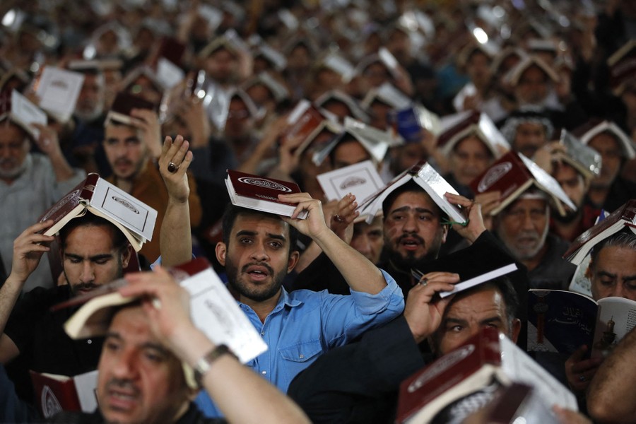 Dozens of men hold books to their head while praying together.