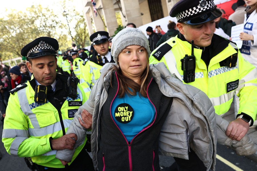 Climate activist Greta Thunberg makes a face while being escorted by two police officers.