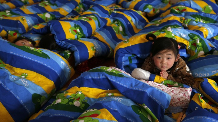 A child looks up at the camera while other children nap around her.