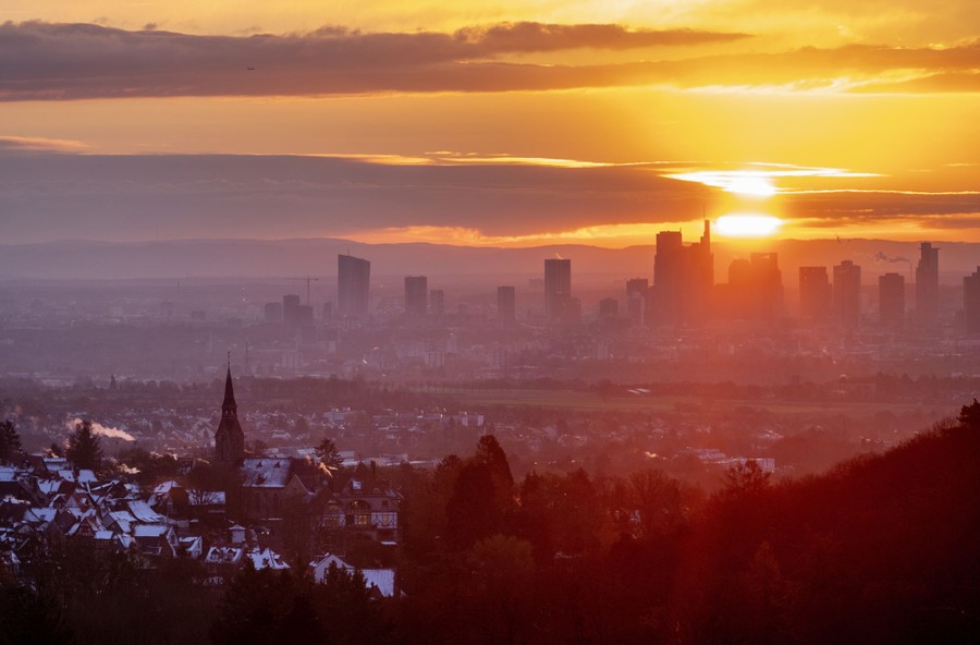 The sun rises behind tall city buildings, seen from a distance.