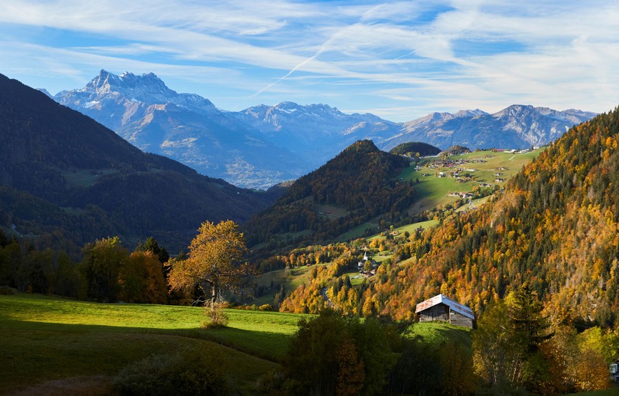 A landscape view of autumn colors and green fields among tall Swiss mountains.