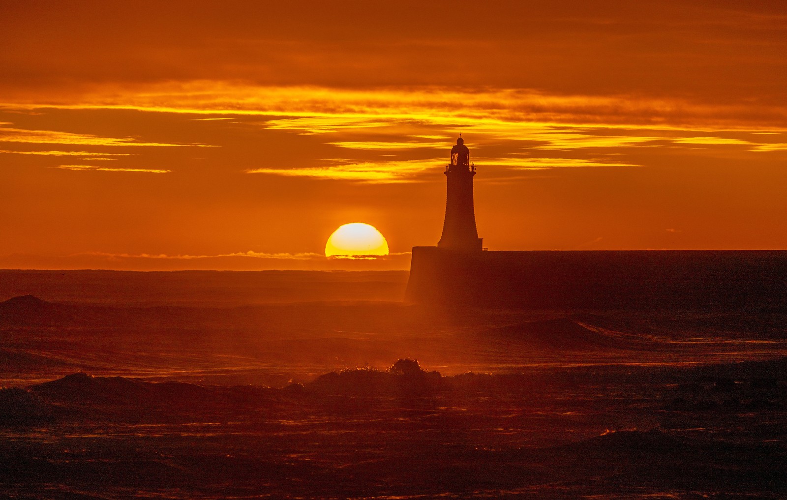 The sunrise, seen behind a lighthouse on a shoreline