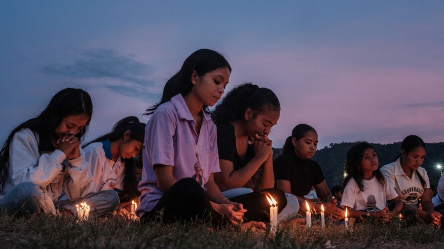 A half-dozen mourners are seen sitting on the ground among lit candles.
