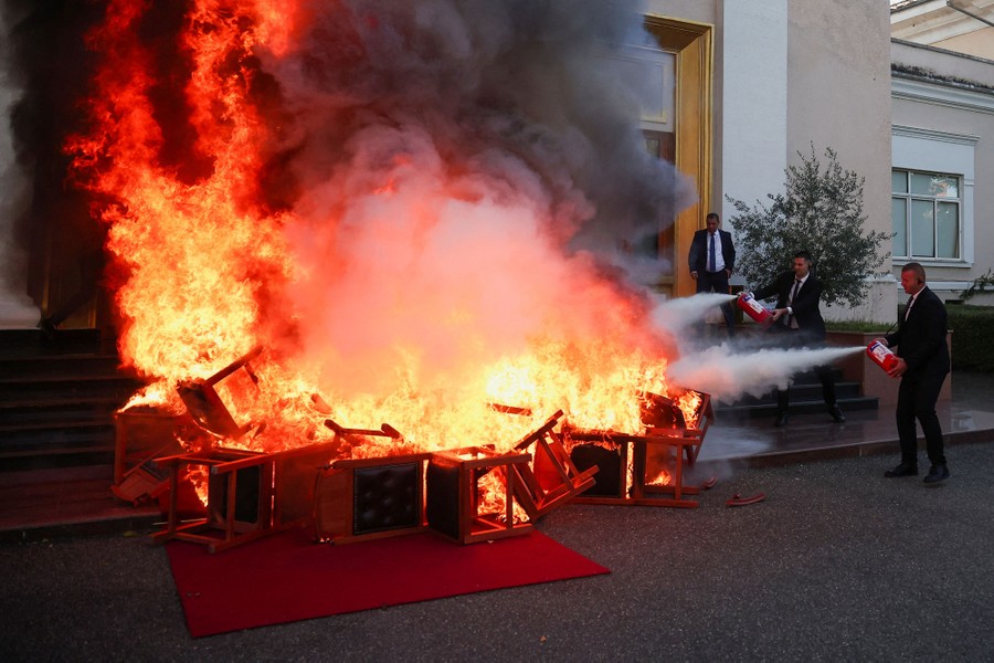 Two people use handheld fire extinguishers to try to put out a fire, which is made up of burning chairs.