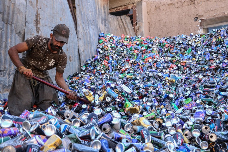 A worker uses a shovel to move a large pile of discarded aluminum cans.
