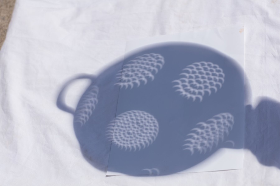 The shadow of a colander, displaying many overlapping crescents—images of a partly-eclipsed sun seen through its many holes.
