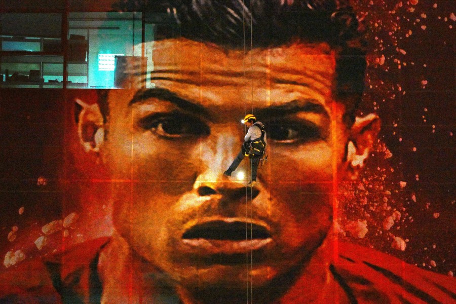 A worker hangs along a wall while installing a large picture of Cristiano Ronaldo.