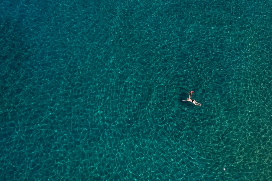 An aerial view of a person swimming in blue-green water