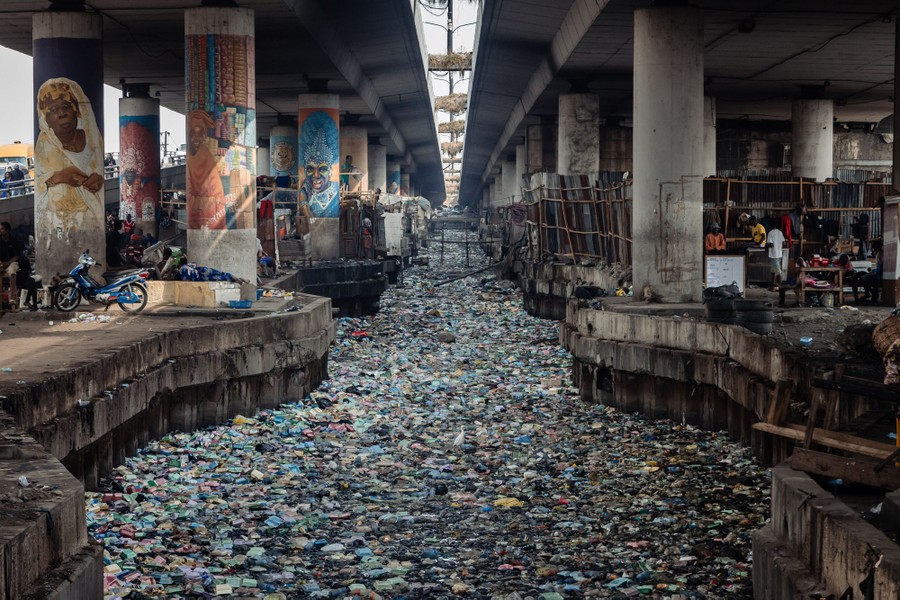 A view of a polluted canal beneath an overpass, filled with styrofoam and plastic