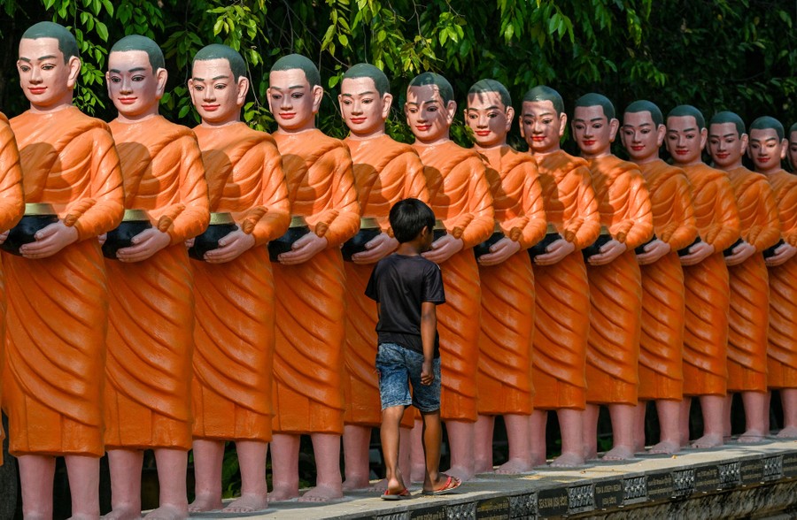 A boy walks past many identical statues of Buddhist monks.