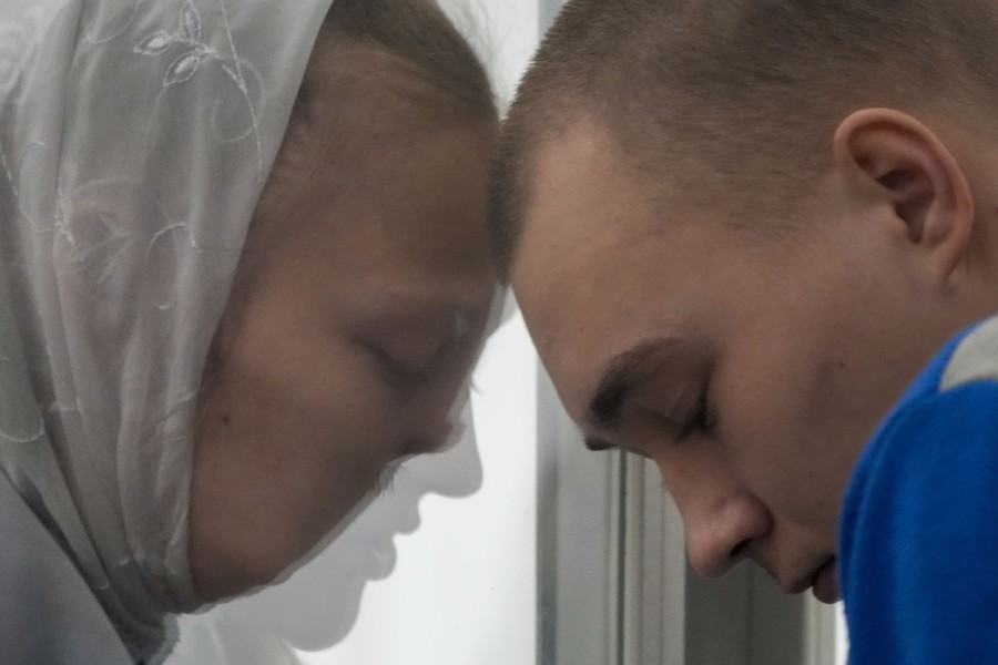 Two people lean their heads close together, separated by glass.
