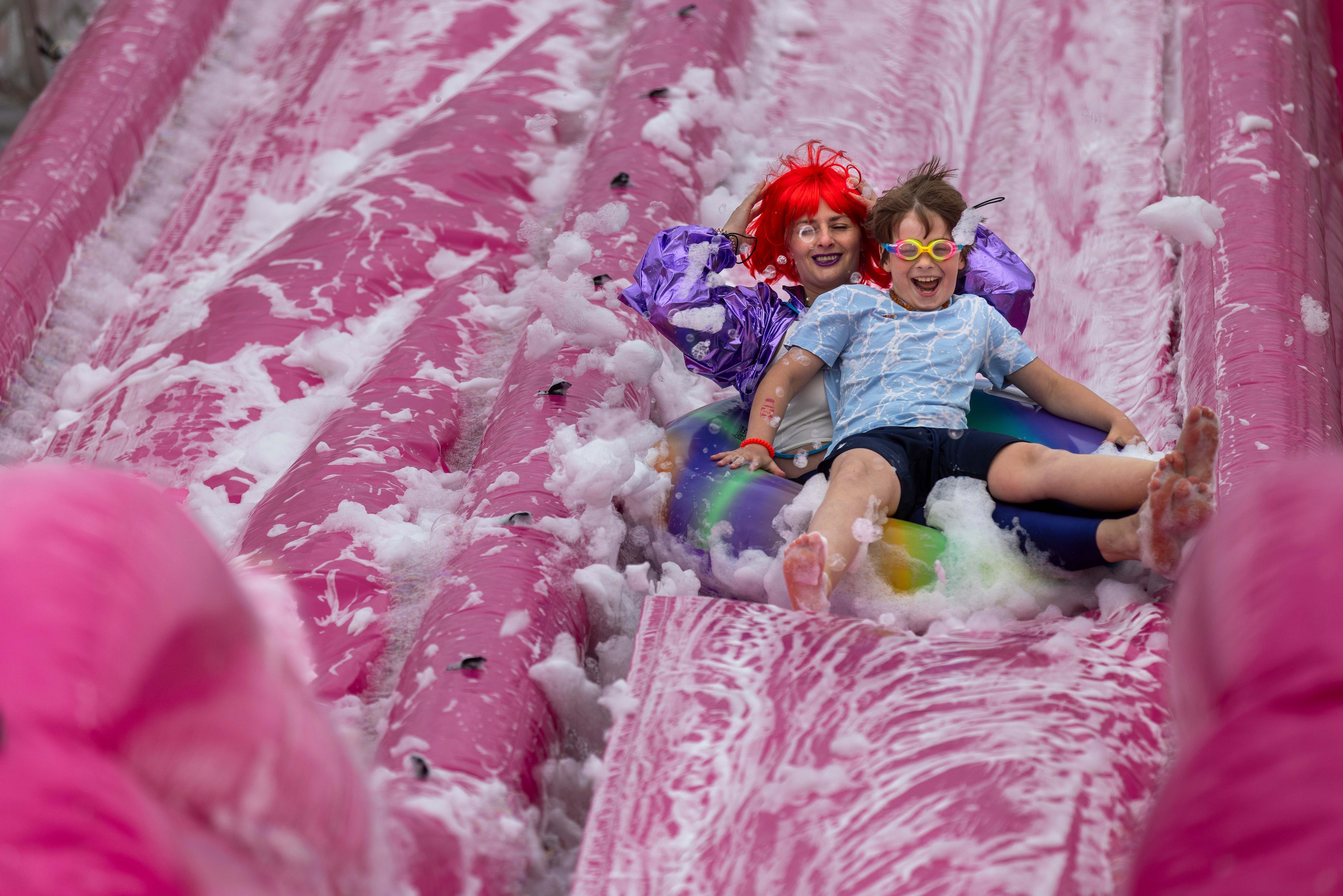 Two people smile as they slip down a sudsy water slide.