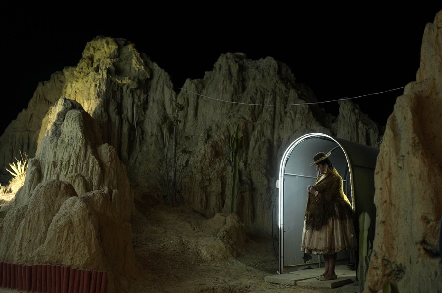A person stands beneath a small arch, near rock formations, at night.