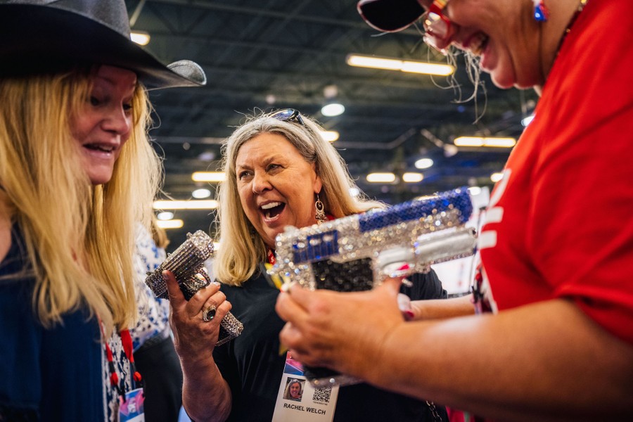 Several women at a convention enjoy themselves while handling what look to be rhinestone-encrusted replica handguns.
