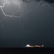 Color photograph of a huge lightning formation lighting up the night sky above an oil tanker