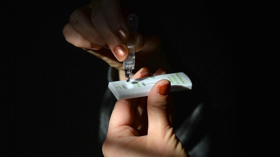A hand drops liquid from a dropper onto a COVID test.