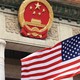 A photograph of an American flag flying under the National Emblem of the People's Republic of China
