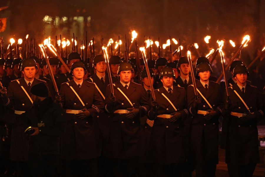 Army soldiers march at night while carrying lit torches.