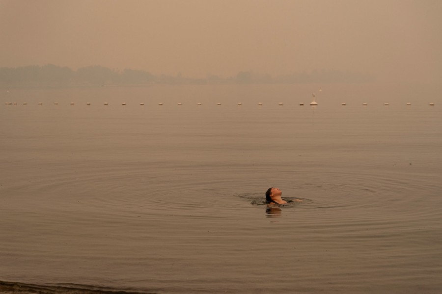 A person swims in a lake beneath an orange, smoke-filled sky.
