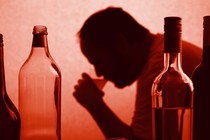A silhouette of a man drinking from a cup next to bottles of wine and liquor