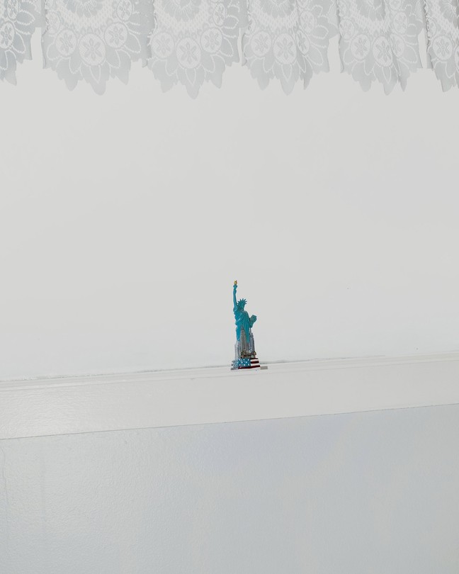 A color photograph of a painted Statue of Liberty souvenir on a windowsill during a snowstorm