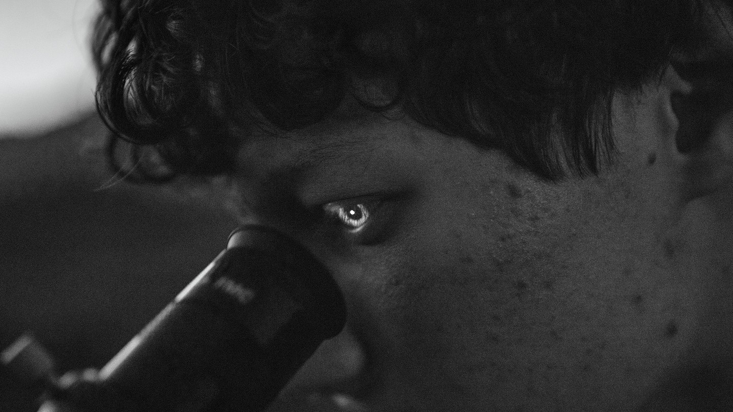 black-and-white photo of person looking into lens of telescope with reflected image lighting up the iris of their eye
