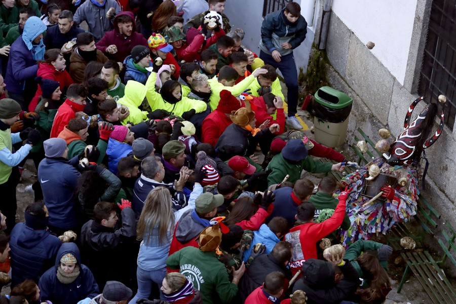 A crowd of people throws turnips at a costumed person sitting on a bench.