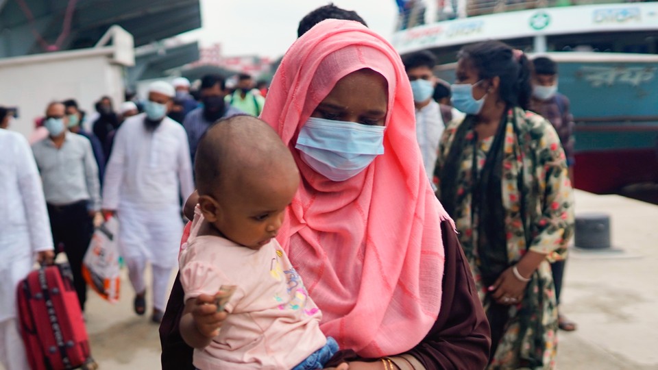 A photograph of a mask-wearing woman carrying a child.