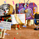 An illustration of a claymation TV, disco ball, microphone, book with a sash, and a clappberboard with legs sitting on top of a wooden platform