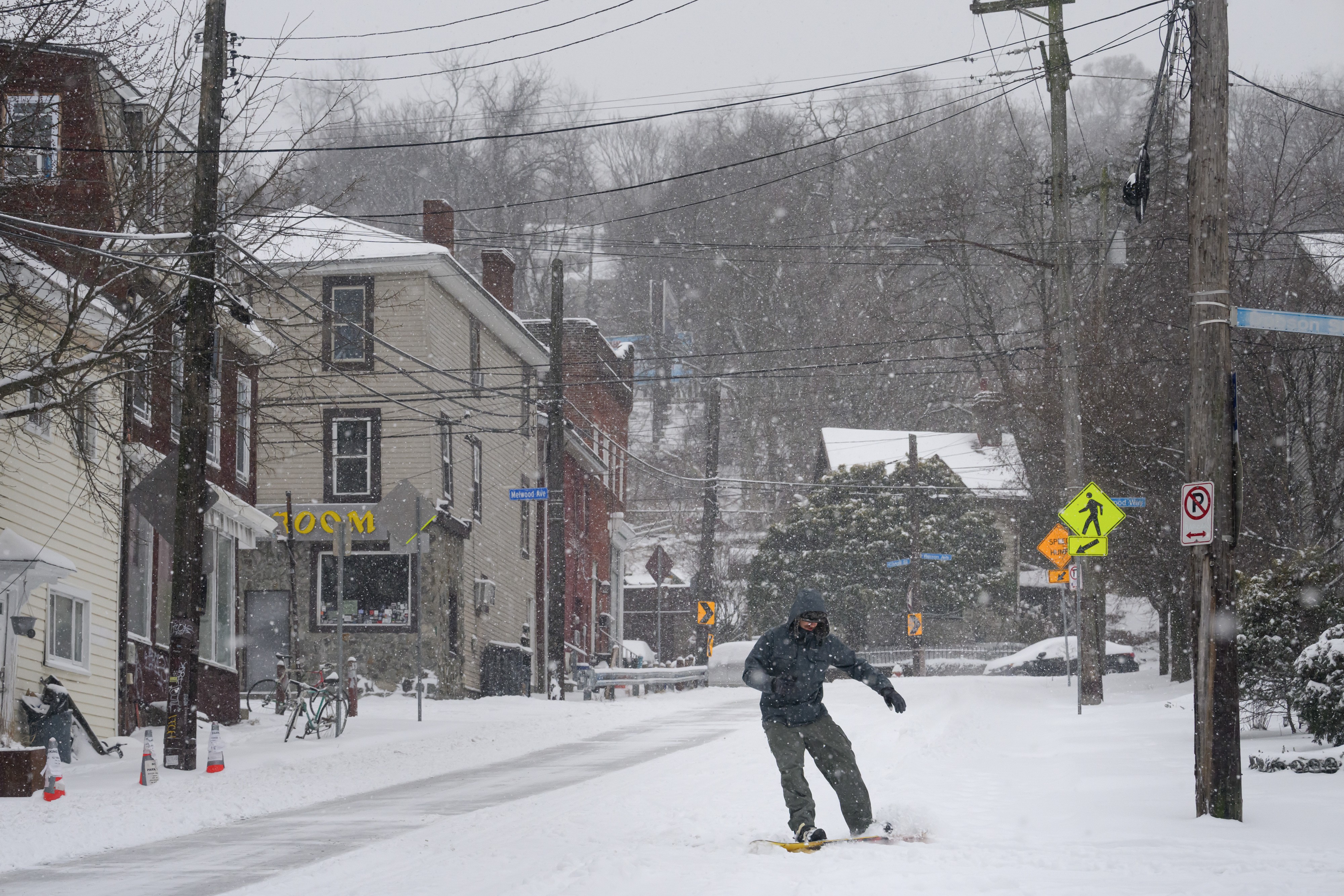 A person snowboards down a snowy street.