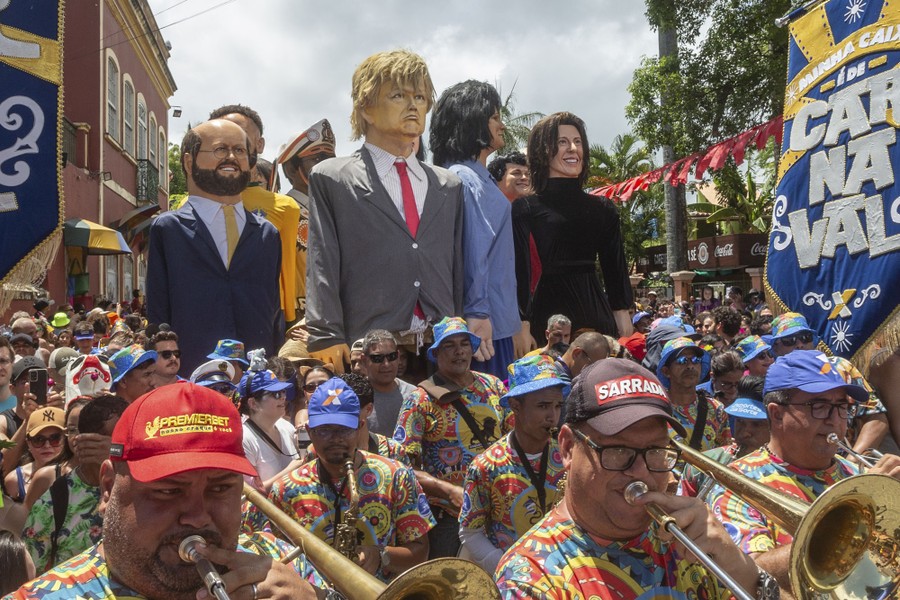 Performers march in a parade, carrying several large puppets