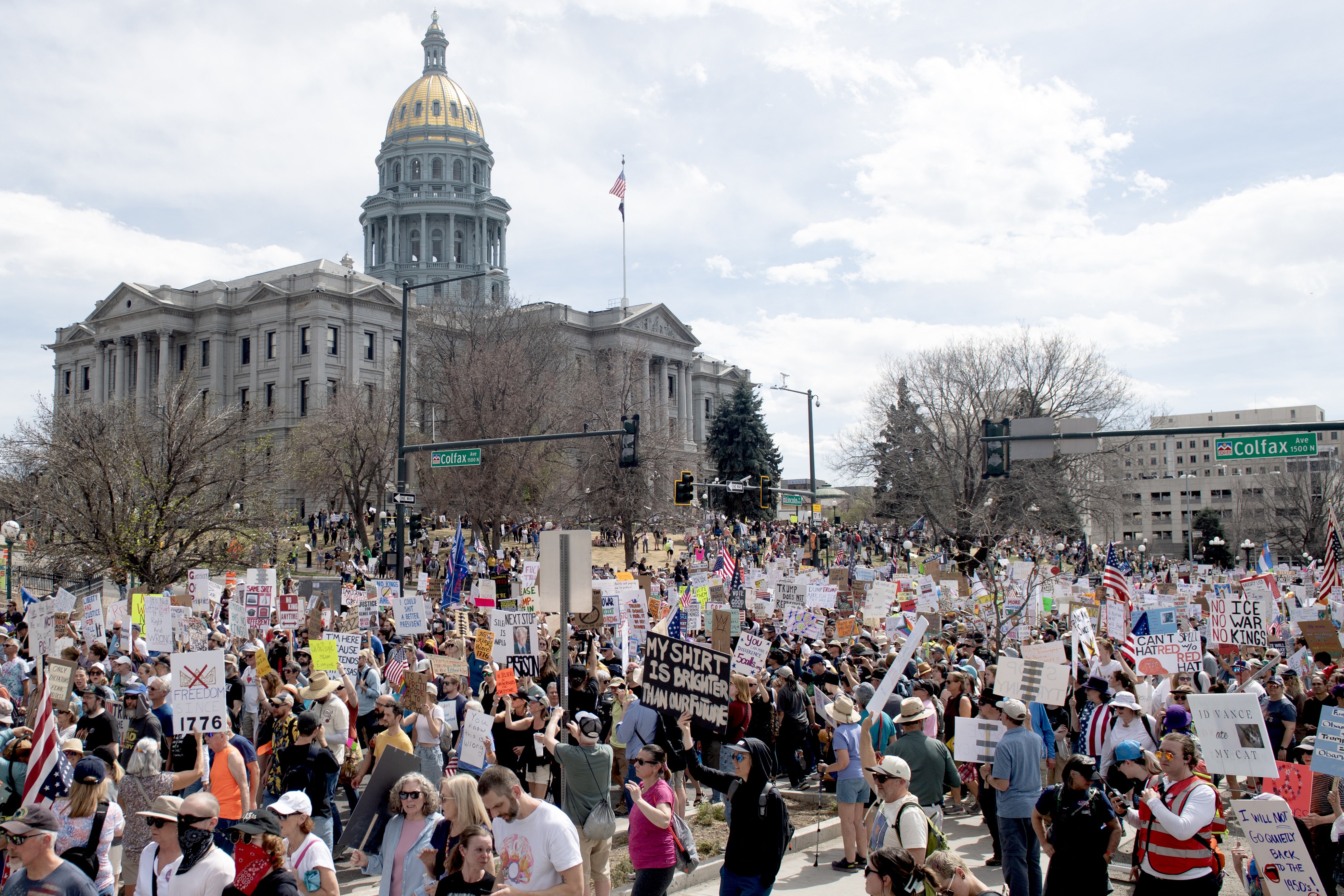A large group of protesters marches outside a state capitol building.